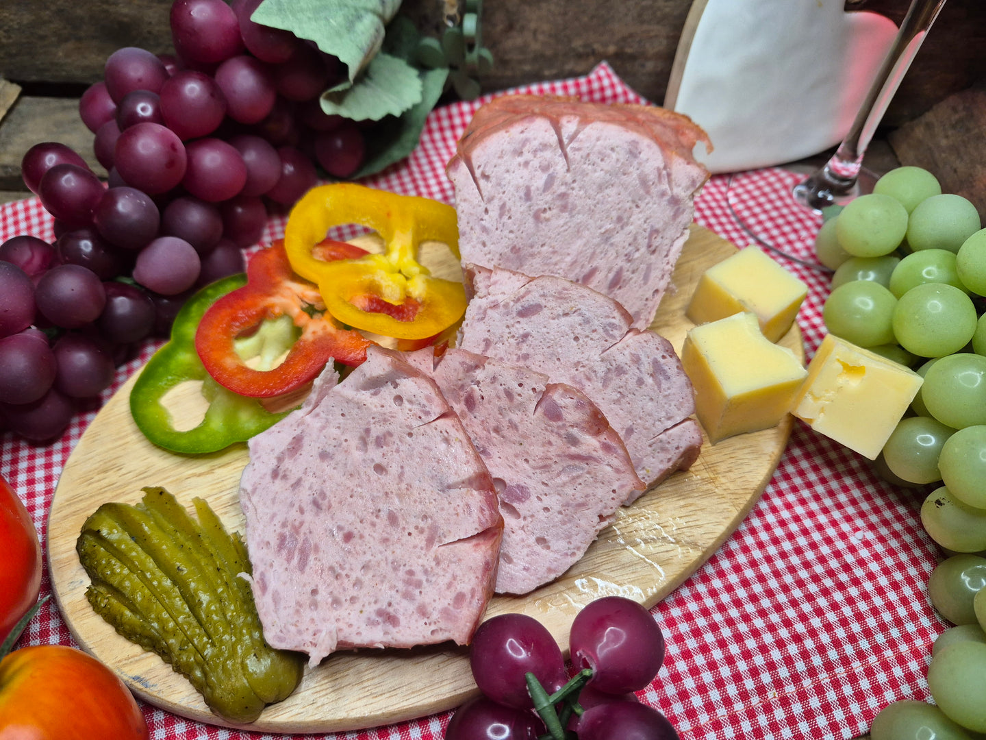 Leberkäse geschnitten auf Holzbrett mit Trauben und Gemüse