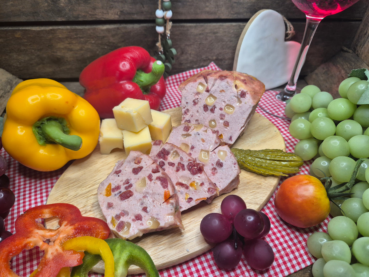 Geschnittener Pizza Leberkäse auf Holzbrett mit Trauben und Gemüse dekoriert
